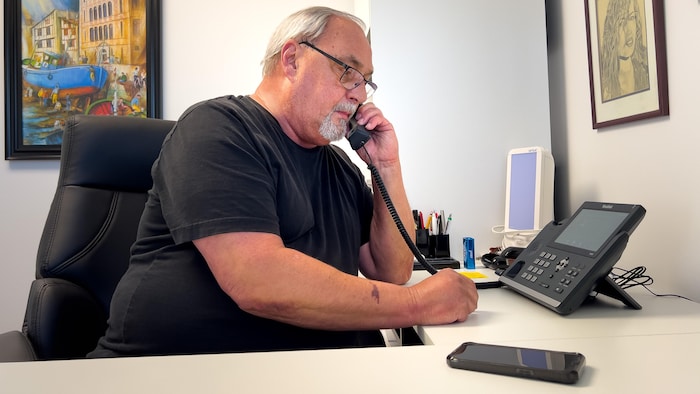 Le directeur est assis à son bureau et parle au téléphone.