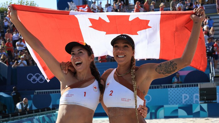 Les joueuses de volleyball de plage Melissa Humana-Paredes et Brandie Wilkerson brandissent le drapeau du Canada en célébrant leur victoire