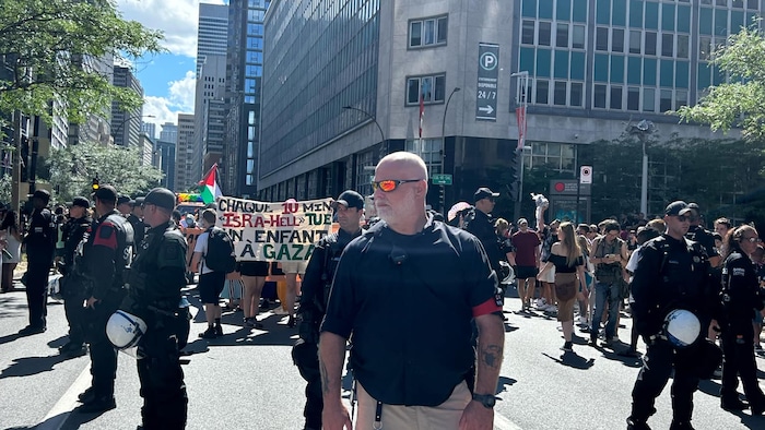 Des membres d'une escouade de sécurité publique sont debout devant des manifestants dans une rue.