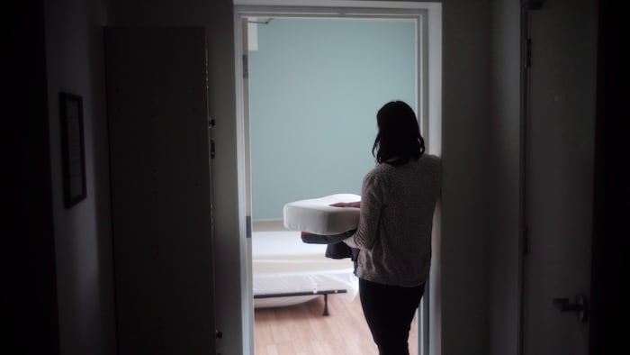Une femme qui transporte de la literie s’apprête à entrer dans la chambre d’un refuge pour femmes violentées.