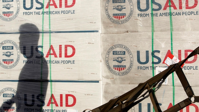 L'ombre d'un homme apparaît sur des caisses affichant l'inscription USAID.