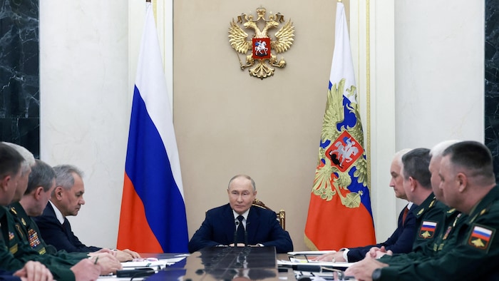 Vladimir Putin sits at the end of a table surrounded by generals.