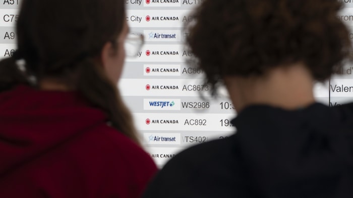 Deux femmes, de dos, regardent une liste de vols sur un écran.