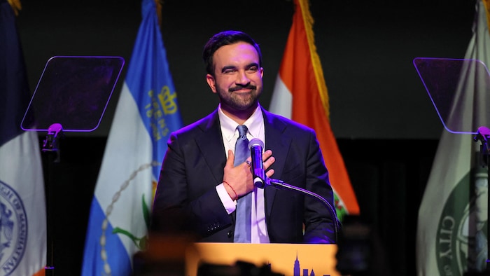 Zohran Mamdani, main sur le cœur, s'adresse à ses partisans en souriant.