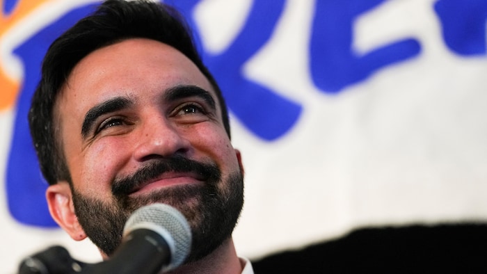 Gros plan d'un jeune homme barbu, souriant, devant un micro.