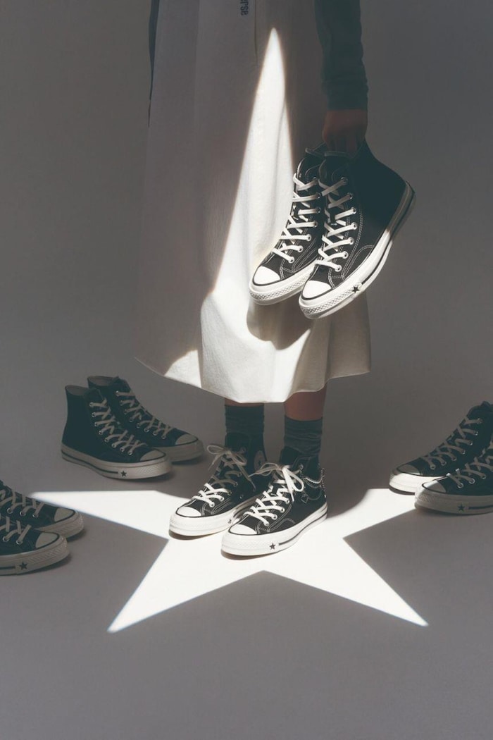 Le bas du corps d'une femme en jupe tenant des souliers, debout au milieu d'une projection lumineuse en forme d'étoile.