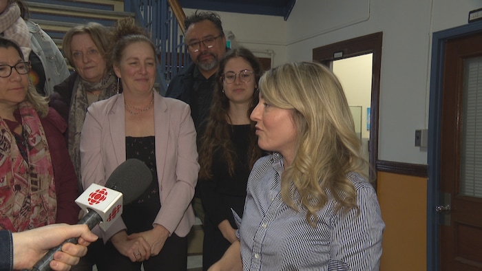 Mélanie Joly parle dans un micro et plusieurs personnes la regardent. 