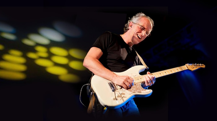 L'homme joue de la guitare sur scène.