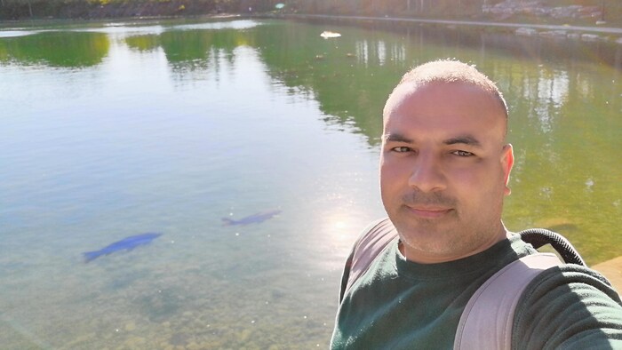 رجل يقف بحيرة صغيرة في متنزه وتبدو سمكتان في الماء.