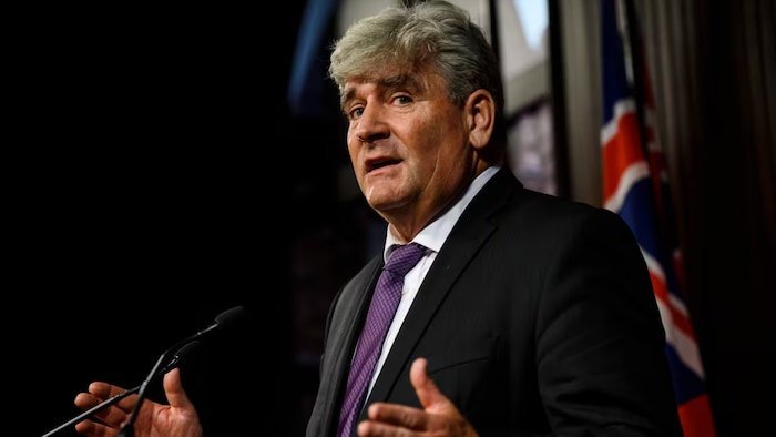 John Fraser qui parle dans une salle avec le drapeau de l'Ontario en arrière-plan.
