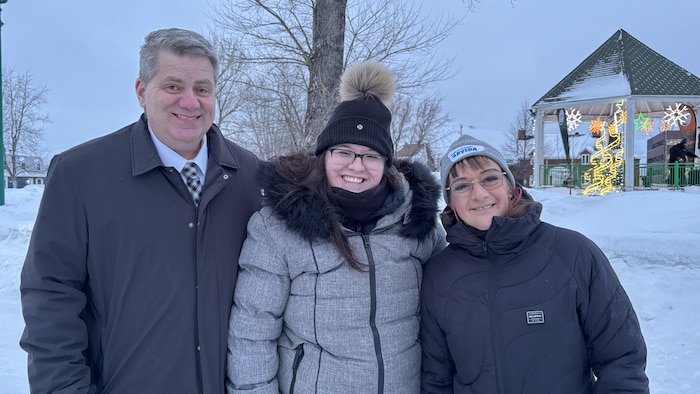un homme et deux femmes, à l'extérieur durant l'hiver, sourient pour la caméra