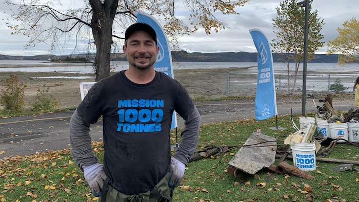 Jimmy Vigneux regarde l'objectif. Derrière lui, les déchets ramassés un peu plus tôt. Il est devant la rivière Saguenay.