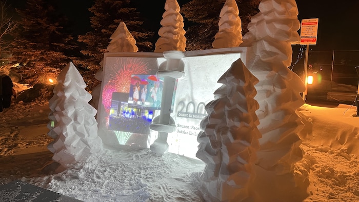 Une sculpture sur neige montre des arbres et un livre ouvert rétroéclairé où des images sont projetées.