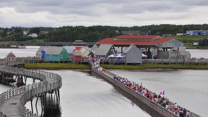 Des gens habillés aux couleurs de l’Acadie marchent sur une passerelle en direction d'une petite île.