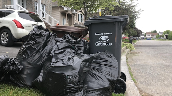 Un bac gris de 120 litres distribué par la Ville de Gatineau avec de nombreux sacs de déchets.