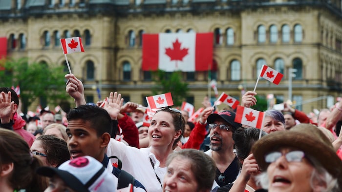 Une foule est rassemblée et brandit des drapeaux canadiens.