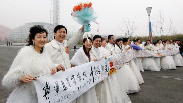 12 Chinese new-married couples hold a wedding banner for the 2008 Beijing Olympic Games with their signatures on during a metro collective wedding ceremony in Nanjing, Sunday Feb. 12, 2006. Romance and marriage have experienced many changes in China after years of breakneck economic growth and looser social controls. The  country is now open to Western influences such as the upcoming  Valentine's Day, where couples now celebrate buy giving chocolates, flowers, cards and heading out to dinner da