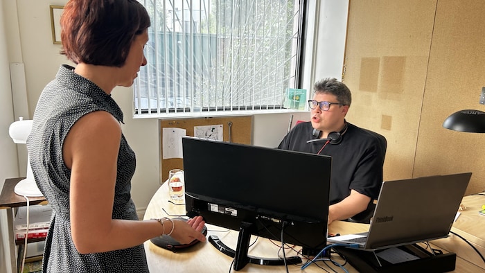 Une dame devant un homme qui est à lad ordinateur.