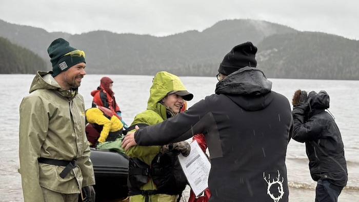 Des personnes descendent d'un zodiac sous la pluie et se font accueillir sur la berge du lac.