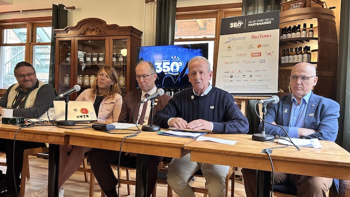 Cinq personnes sont assises à une longue table où sont placés des micros. 