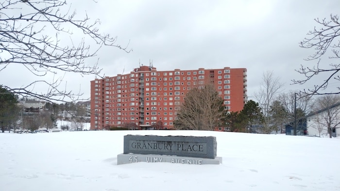 Un gros bâtiment résidentiel de 10 étages entouré de neige et devant lequel il y a un bloc de marbre avec les mots « Granbury Place » et une adresse.