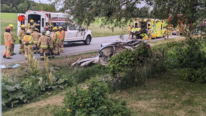 Des ambulanciers et des pompiers devant une scène d'accident de voiture.