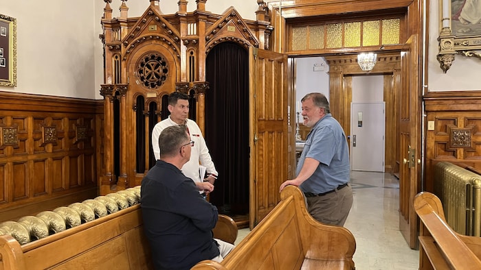 Trois hommes discutent dans une église.