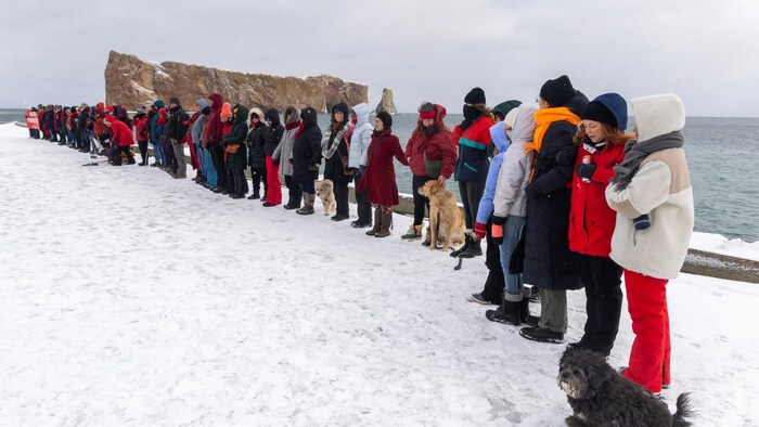 Des gens se tiennent par les mains et forment une ligne sur un quai devant le rocher Percé.