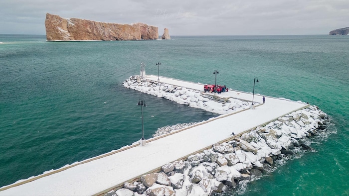 Vue aérienne du quai de Percé. Des gens y forment un cercle. Au loin, le rocher Percé.
