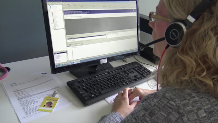 Une femme travaillant à un ordinateur porte un casque muni d'un micro pour répondre aux appels du public.