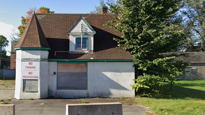 Un petit bâtiment abandonné, ses fenêtres barricadées, avec une affiche interdisant de stationner.