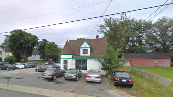 Un petit bâtiment brun, blanc et vert, avec plus d'une dizaine de voitures stationnées n'importe comment autour.