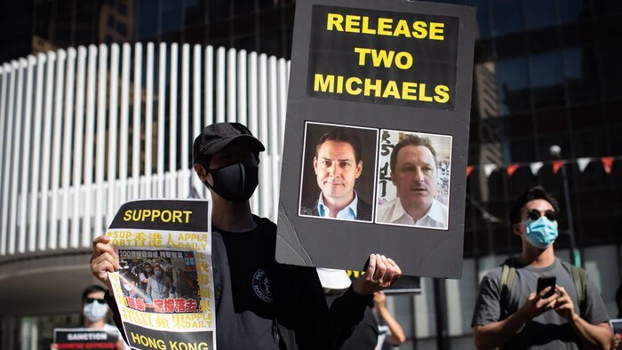 A person holds a sign with photographs of Michael Kovrig and Michael Spavor, who have been detained in China since December, 2018, as people gather for a rally in support of democracy in Hong Kong in Vancouver, B.C., Sunday, Aug. 16, 2020.