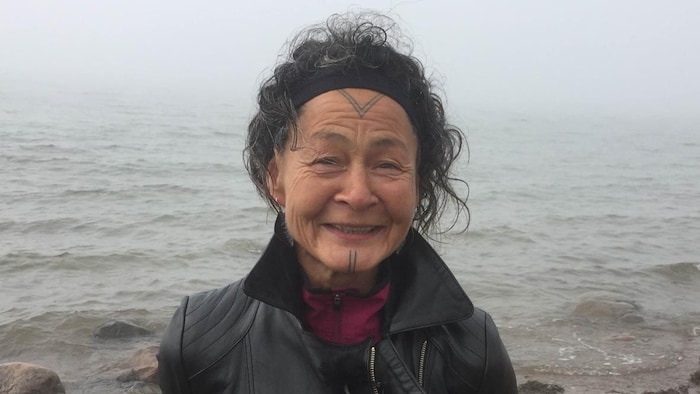 Une femme regarde la caméra en souriant, devant un cours d'eau.