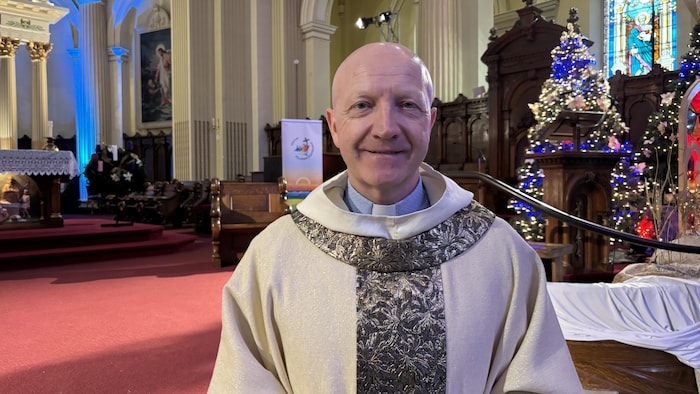 un curé habillé avec son costume de messe dans une église décorée pour noël