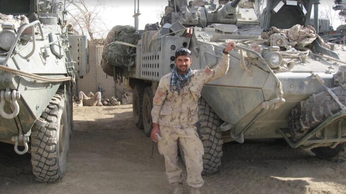 عبد الحكيم عزيزي يقف قرب ناقلة جند كندية في أفغانستان.