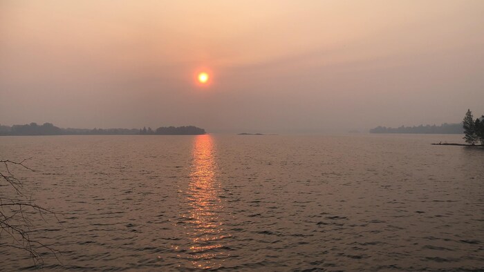 Vue sur un plan d'eau alors que le soleil se lève. Le ciel est assombri par de la fumée.