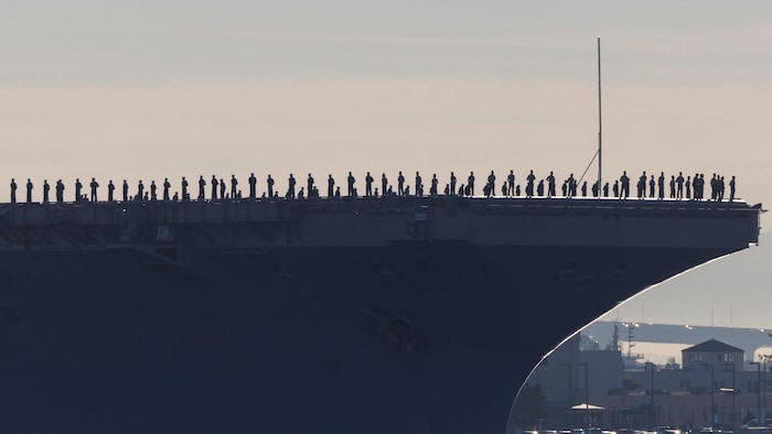 Les silhouettes des marins d'un porte-avions sont alignées sur le pont du navire.