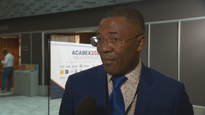 Augustin Bala est en entrevue devant une bannière de l'événement Acabex.