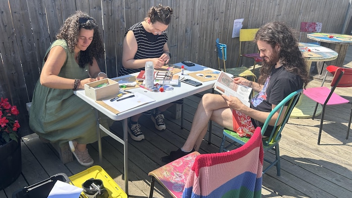 Trois personnes dessinent sur une table extérieure.