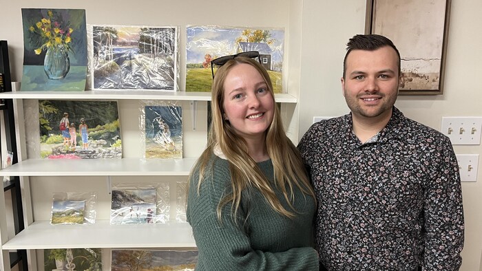 Corine Morin-Parent et Pierre-Louis Gilbert Gauthier posent devant des œuvres de Marcelle Lemay exposées dans leur magasin de meubles.
