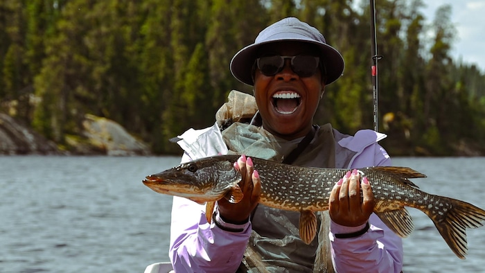 Une femme sourit avec un poisson qu’elle a pêché dans les mains.