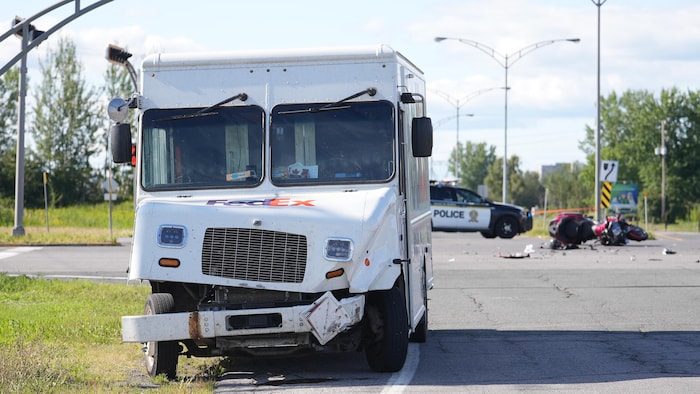 Un camion FedEx a le devant amoché, derrière une moto accidentée est sur la chaussée près d'un véhicule de police.