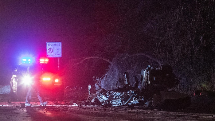 Une carcasse de voiture et une voiture de police sur une route la nuit.