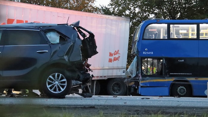 Un VUS gris, dont l’arrière est lourdement endommagé, se trouve devant une semi-remorque blanche, à proximité d’un autocar bleu à deux étages, sur les lieux d’un carambolage sur la route 99.
