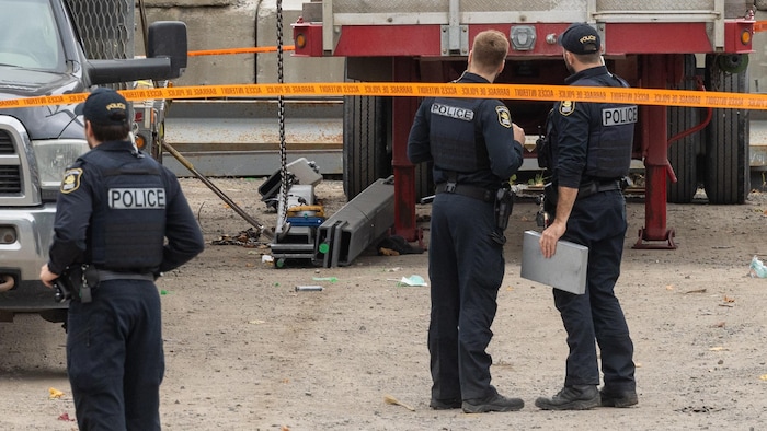 Des policiers du SPVQ observent une charge de métal au sol, en dessous d'une remorque de camion. 
