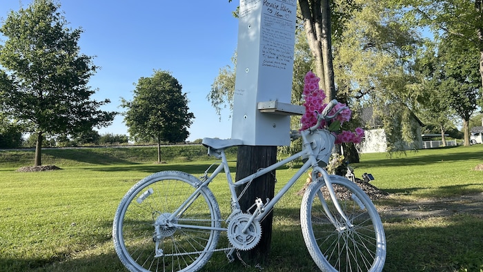 Un vélo peinturé en blanc sur lequel se trouve un bouquet de fleurs. 