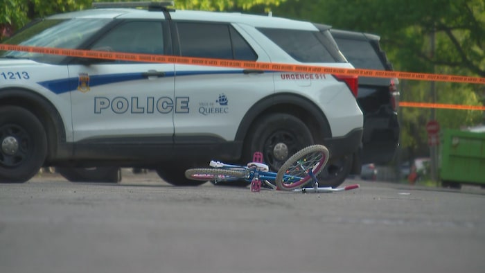 Une bicyclette bleue et rose sur le sol devant un véhicule de police.