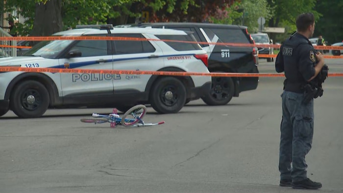 Des voitures de police sont stationnées autour d'une bicyclette rose et bleue sur le sol.
