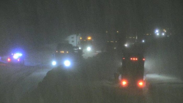 Multiples lumières de phares qui paraissent sur fond de nuit noire, suggérant qu'un camion lourd est sorti de la route et s'est enfoncé dans la neige. 